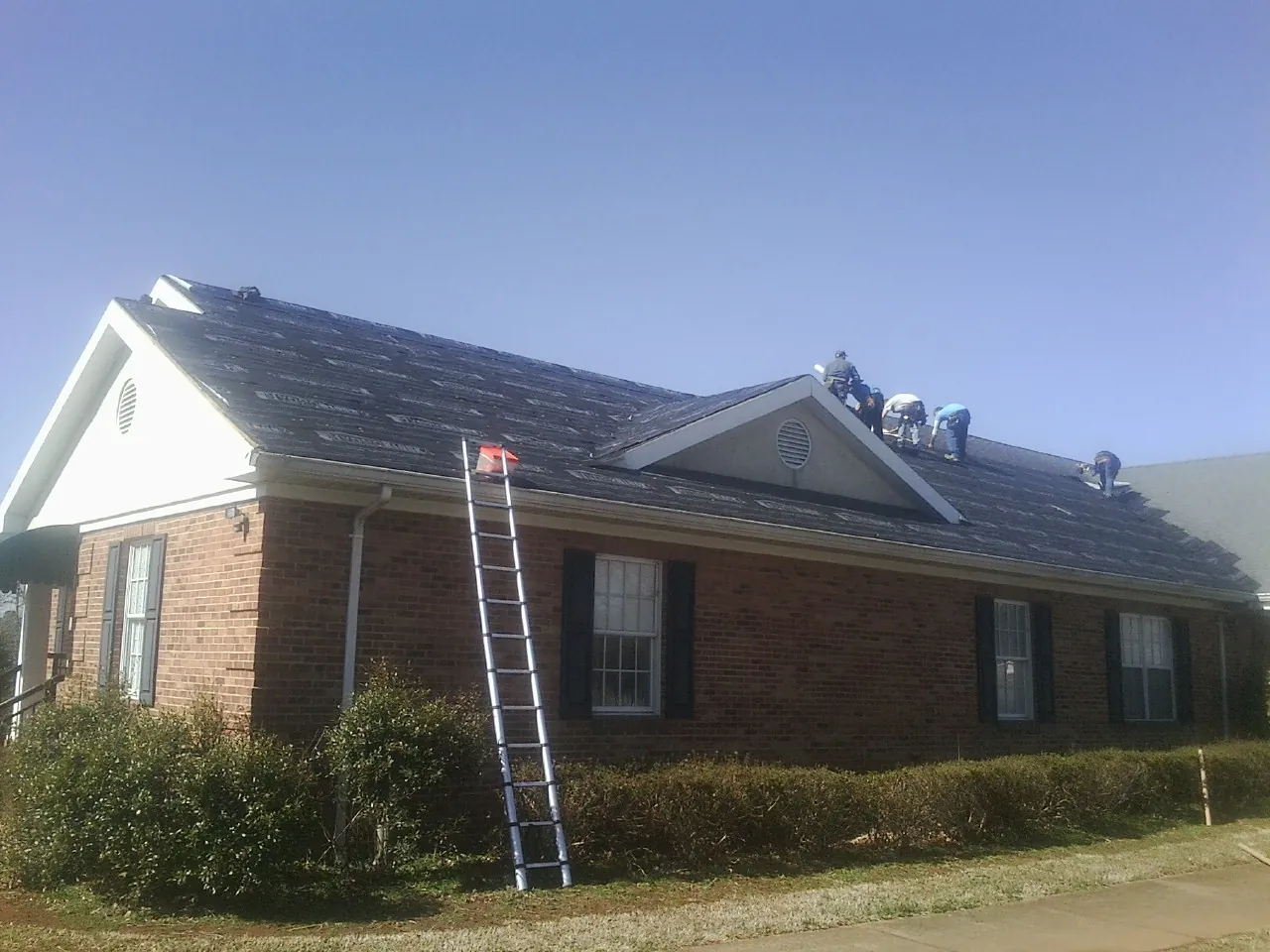 Crew tearing shingles off a brick ranch roof with a ladder set — Metal Roof Repair work by our crew in Voluntown