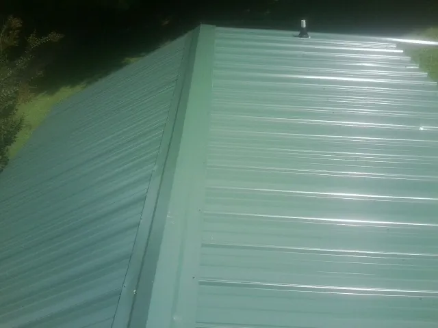 New green metal panels meeting at the ridge of a roof — Flat Roof Repair work by our crew in Voluntown