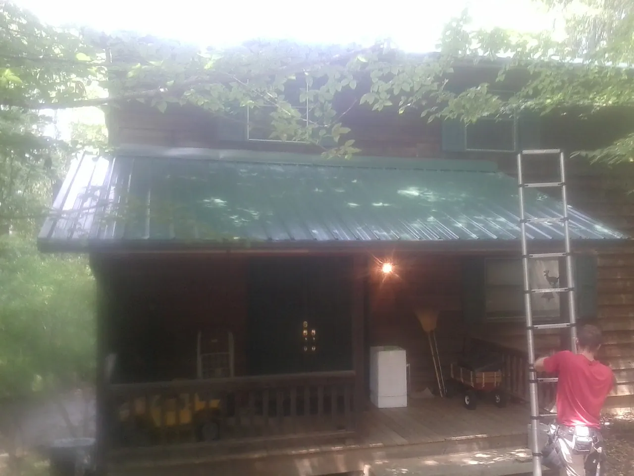 Worker on a ladder at the green porch roof of a wooded cabin in Voluntown