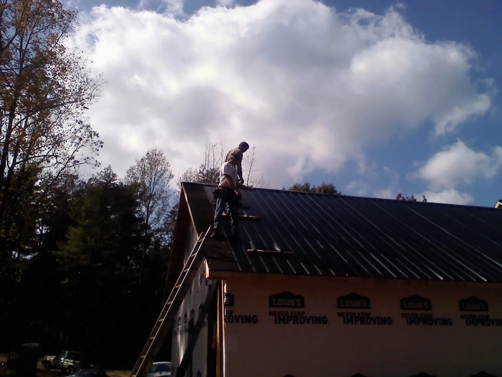 Roofer fastening dark metal panels high against a cloudy sky, from a Roof Inspection job in Voluntown