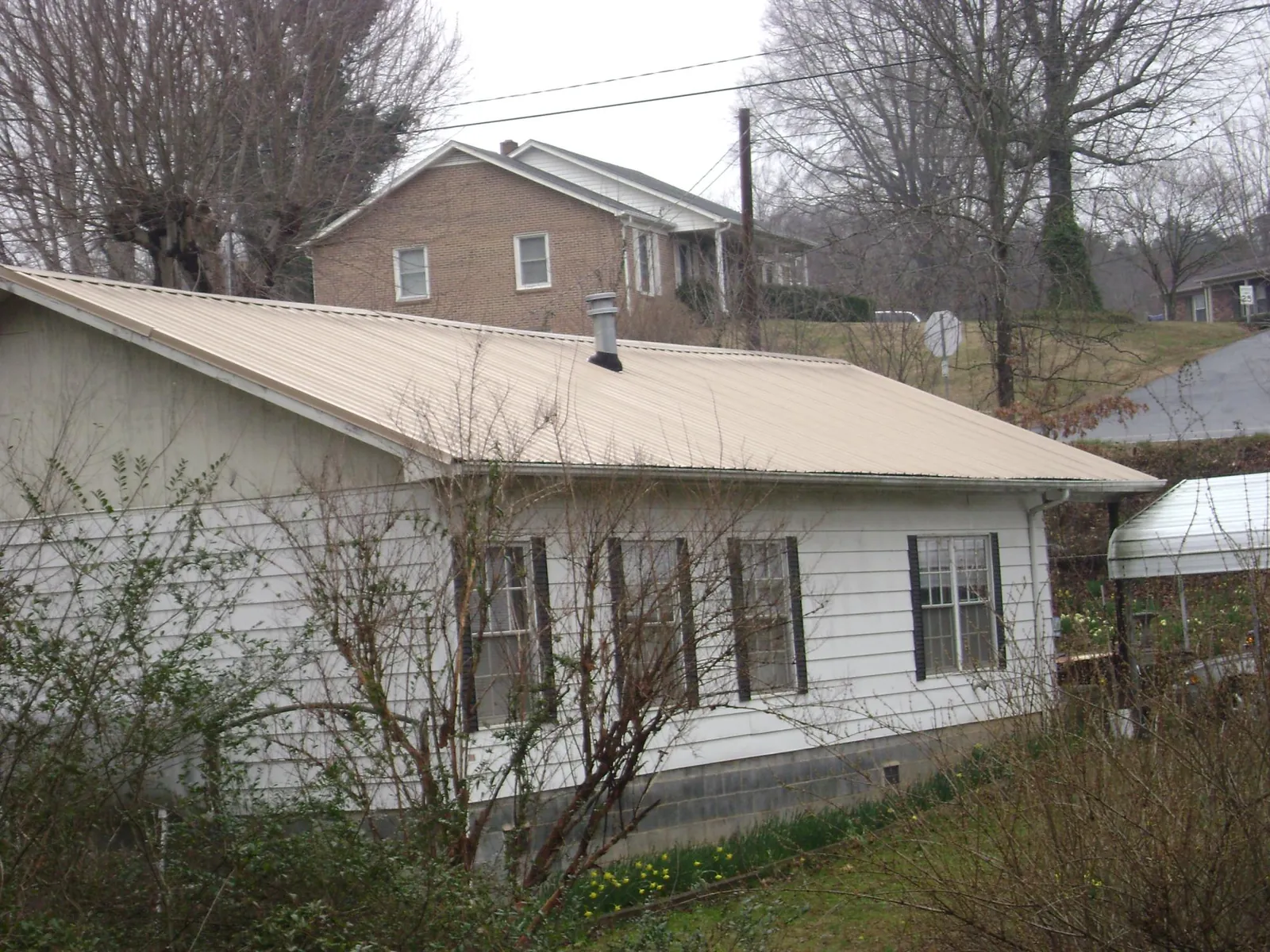 Tan metal roof on a white sided house set into a hillside — Commercial Roofing by Roofing Brothers in Voluntown